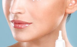 Beautiful woman applying cream treatment on her perfect face on blue